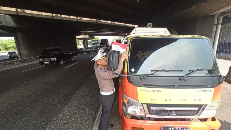 Anggota Dirlantas Polda Jatim membagikan bendera merah putih ke Sopir truk.